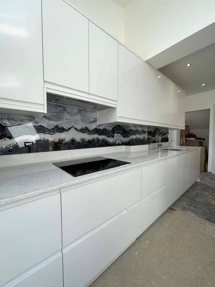 Modern kitchen with bespoke glass splashback featuring mountain wave design, sleek white cabinets, and granite countertop.