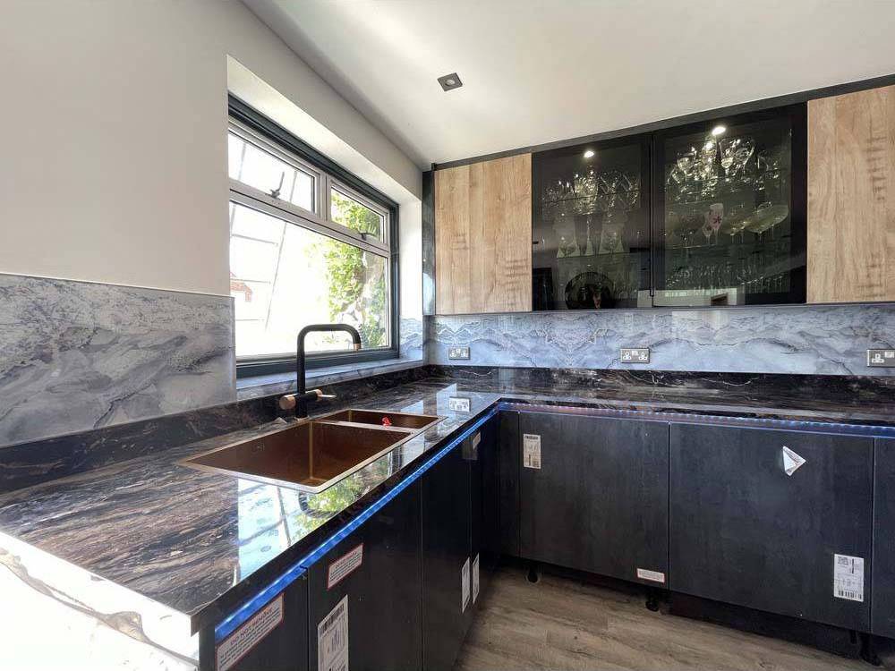 Modern kitchen with black marble countertop, LED-lit glass backsplash, and sleek cabinets