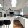 Modern kitchen with bespoke glass splashback featuring ocean sunset design, white cabinets, and skylights