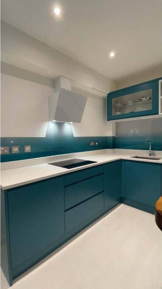 Modern kitchen with teal glass splashback and sleek cabinetry, featuring LED lighting and contemporary design.