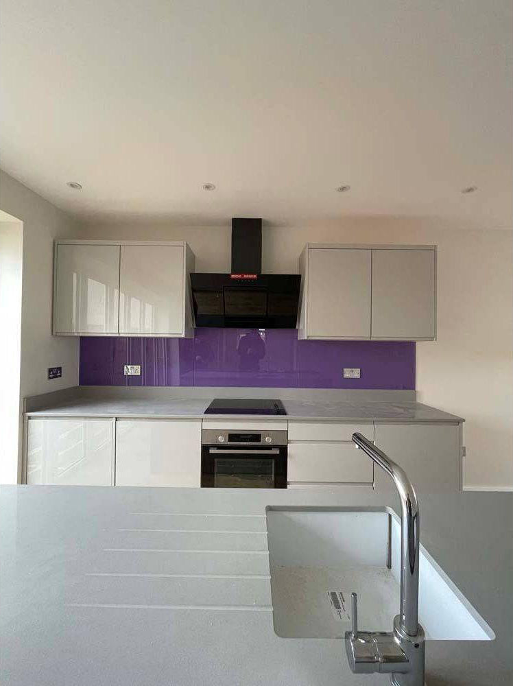 Vibrant purple glass kitchen splashback with modern white cabinets and stainless steel appliances