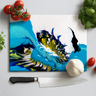 Colorful resin cutting board with blue and yellow design surrounded by cherry tomatoes, garlic, basil, and kitchen knife