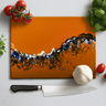 Orange cutting board with abstract black, white, and blue design, surrounded by cherry tomatoes, garlic, basil, and a chef's knife