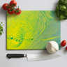 Vibrant yellow and green swirl glass chopping board with chef knife, tomatoes, garlic, and basil