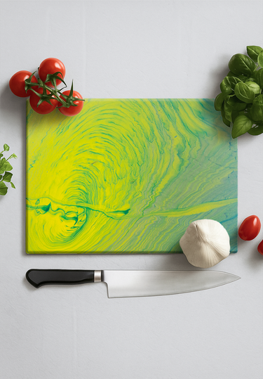 Vibrant yellow and green swirl glass chopping board with chef knife, tomatoes, garlic, and basil