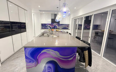 Modern kitchen with purple and silver glass splashback on island, sleek white cabinets, and pendant lights