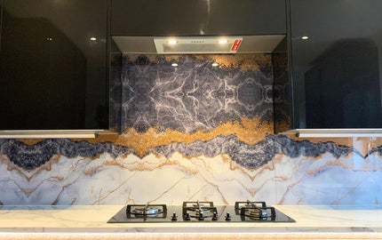 Luxury kitchen with bespoke decorative glass backsplash featuring marble and gold veining, modern black cabinets, and gas hob.