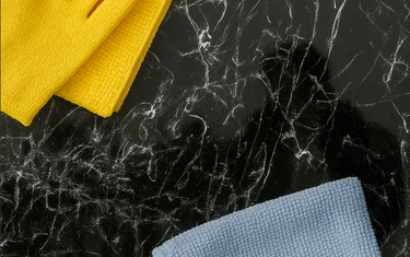 Yellow glove and blue microfiber cloth on black marble surface for cleaning glass surfaces