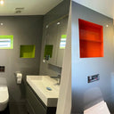 Modern bathroom with vibrant green and orange glass shelves, sleek vanity, and LED-lit mirror