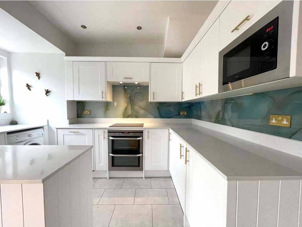 Modern kitchen with bespoke glass splashback in teal marble design, white cabinets, and stainless steel appliances