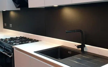 Sleek black glass splashback in modern kitchen with white cabinets and black sink