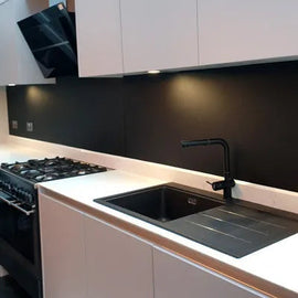 Sleek black glass splashback in modern kitchen with white cabinets and black sink