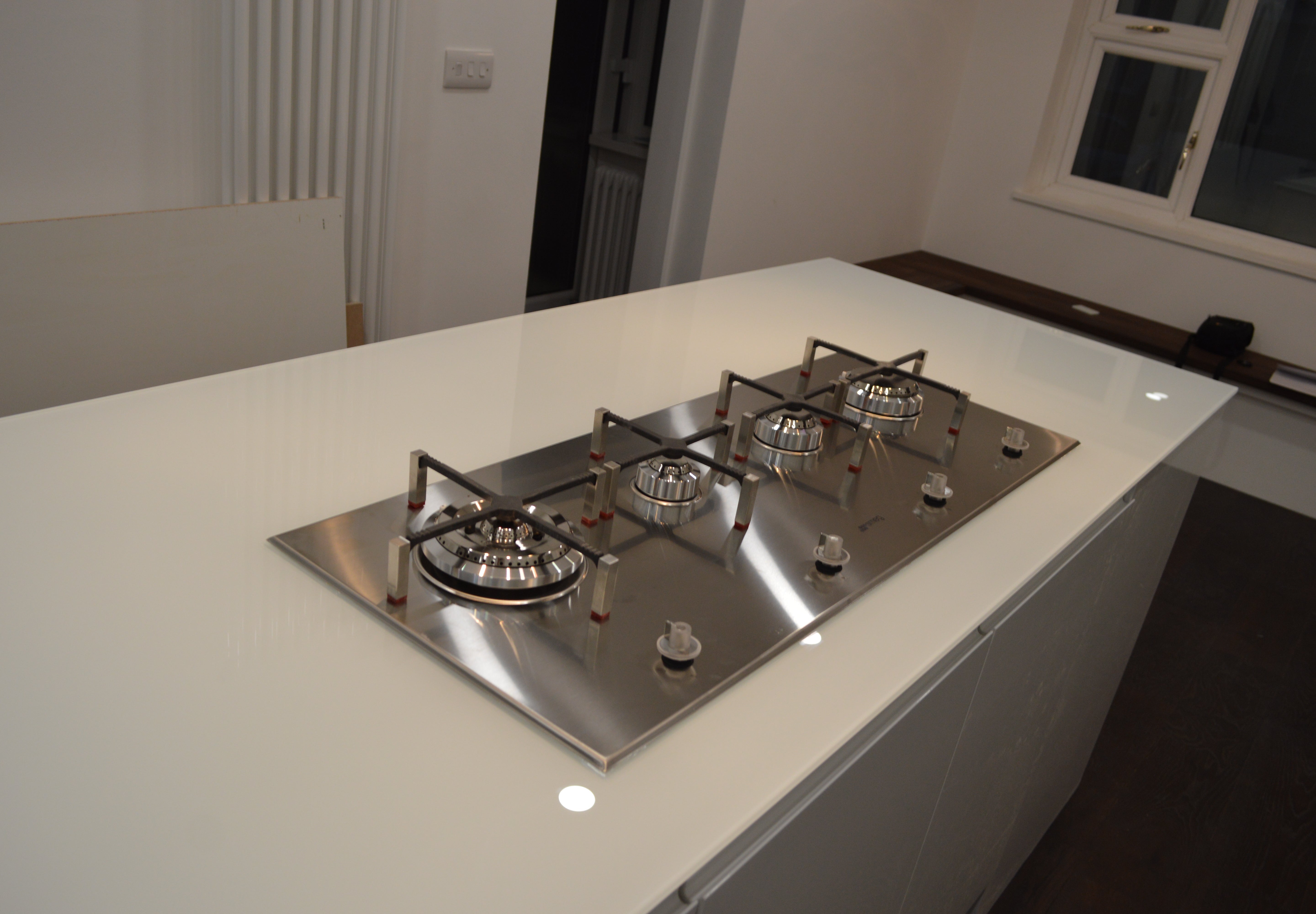 Bespoke white glass kitchen worktop with integrated stainless steel gas hob for luxury residential interiors
