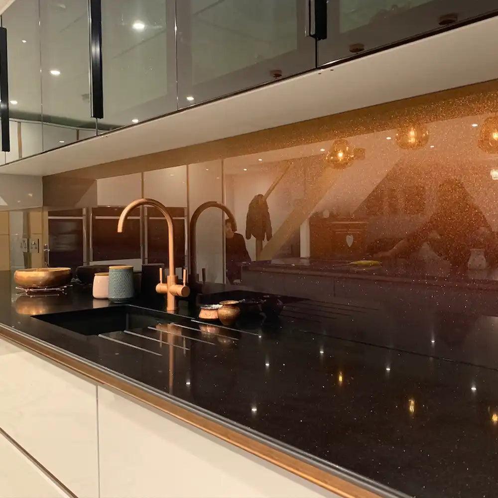 Luxury kitchen with bespoke decorative glass splashback and black countertop, featuring gold accents and modern fixtures.