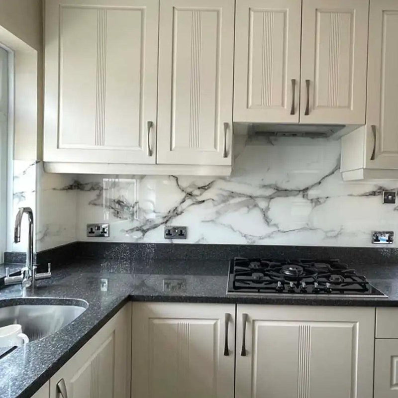 Marble-effect glass splashback in modern kitchen with white cabinets and black granite worktop