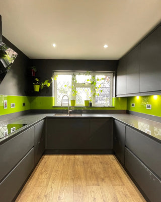 Modern kitchen with vibrant lime green glass splashback, grey cabinets, and wooden flooring.