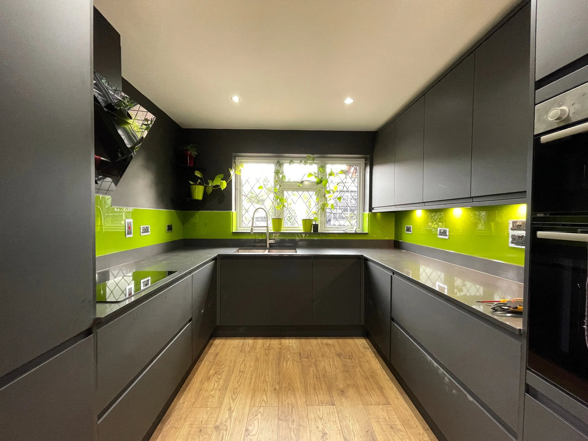 Modern kitchen with vibrant lime green glass splashback, grey cabinets, and wooden flooring