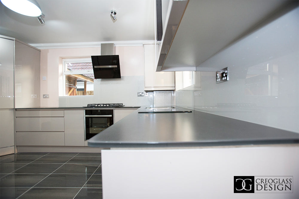 Modern kitchen with sleek glass splashback and glossy white cabinets, featuring contemporary design and clean lines.