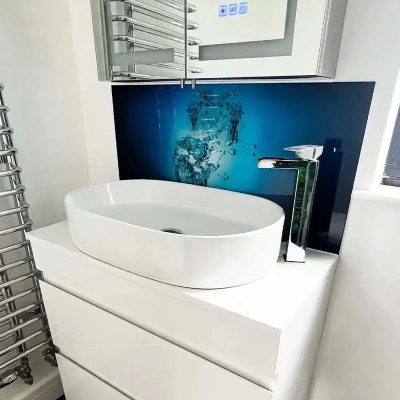 Blue decorative glass splashback with water design behind white basin in modern bathroom