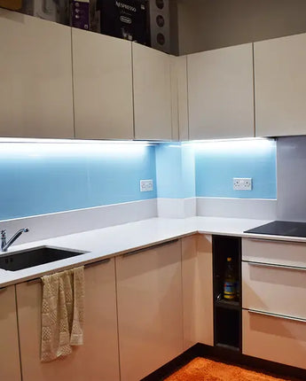Modern kitchen with blue backlit glass splashback and sleek white cabinets