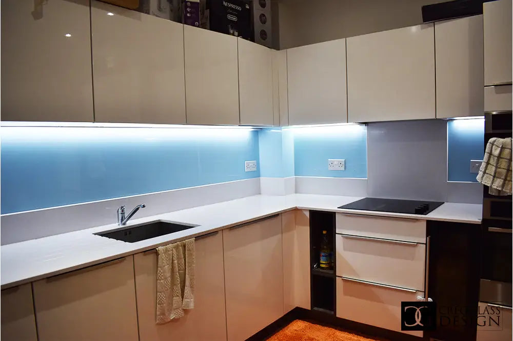 Modern kitchen with LED backlit blue glass splashback and sleek white cabinets