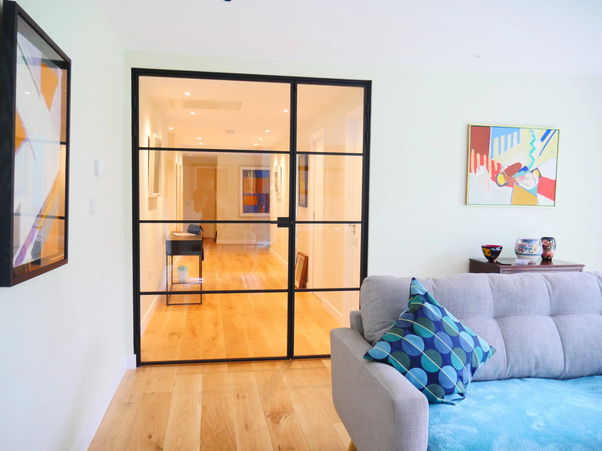 Black-framed glass partition in modern living room with wooden floors and grey sofa