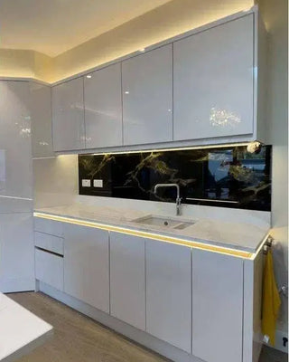 Modern kitchen with sleek white cabinets and black marble splashback, featuring LED lighting and a stainless steel sink.