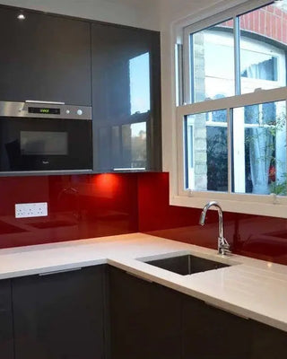 Modern kitchen with glossy red glass splashback, sleek black cabinets, and white countertop near window