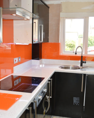 Vibrant orange glass splashback in modern kitchen with black cabinets and white countertop