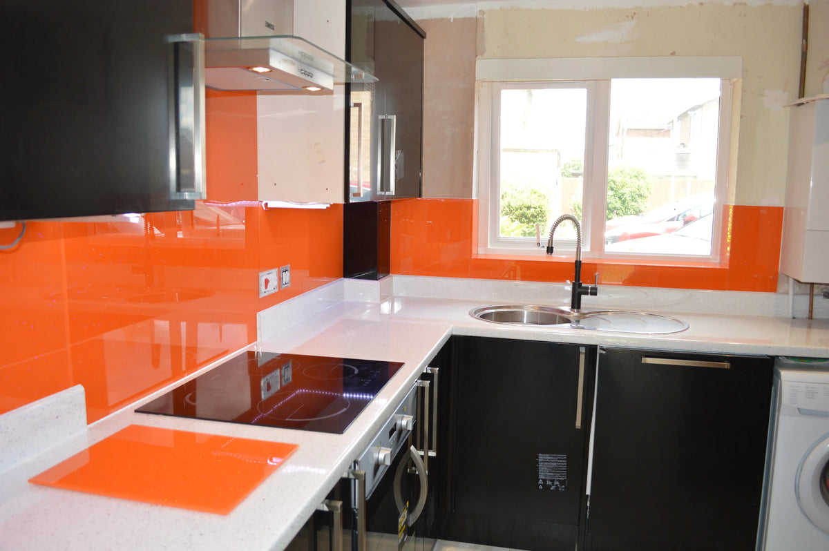 Vibrant orange glass splashback in modern kitchen with black cabinets and white countertop