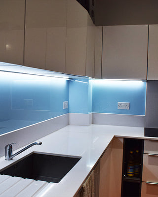 Modern kitchen with blue backlit glass splashback, white countertops, and sleek cabinets