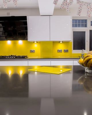 Vibrant yellow glass splashback in modern kitchen with white cabinets and fruit bowls