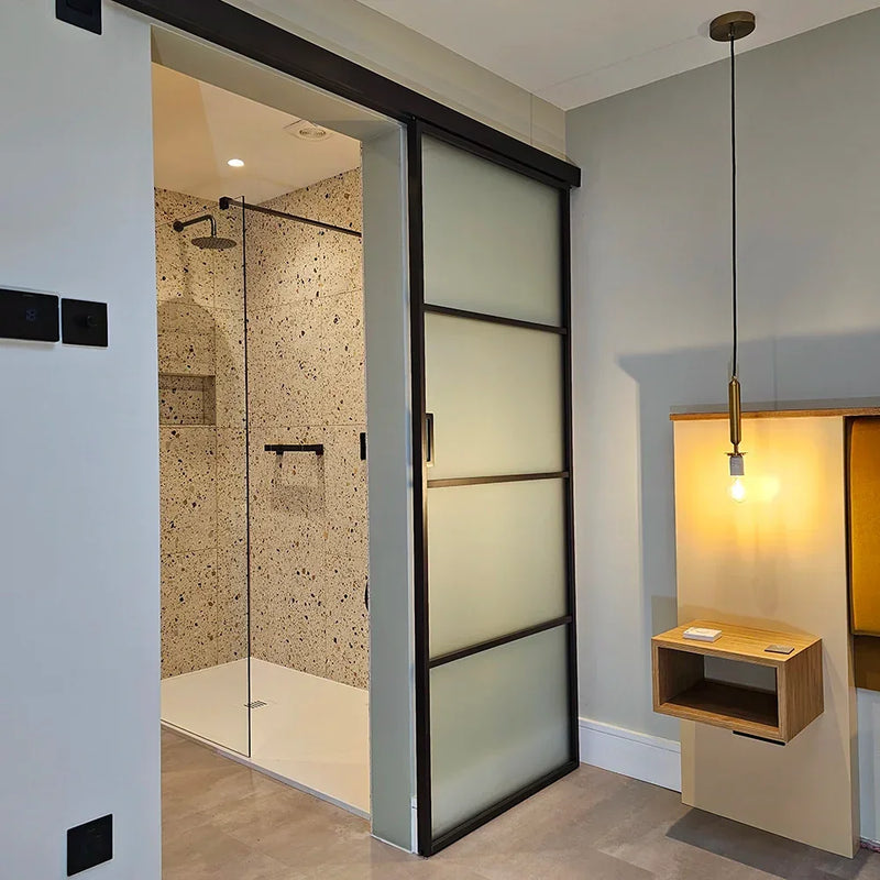 Modern frosted glass sliding door with black frame, leading to luxury bathroom with terrazzo shower