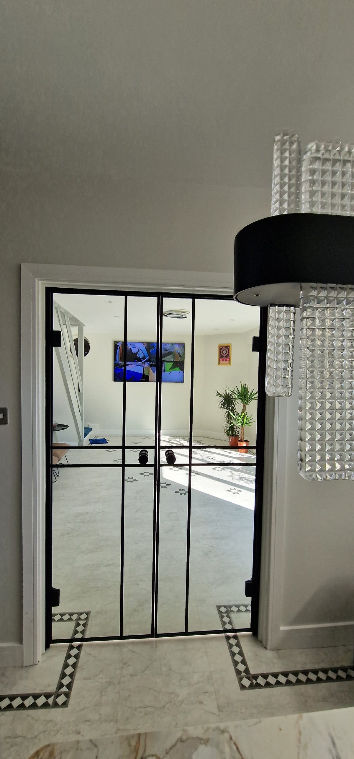 Modern interior with black double hinged glass doors, white walls, tiled floor, and chandelier