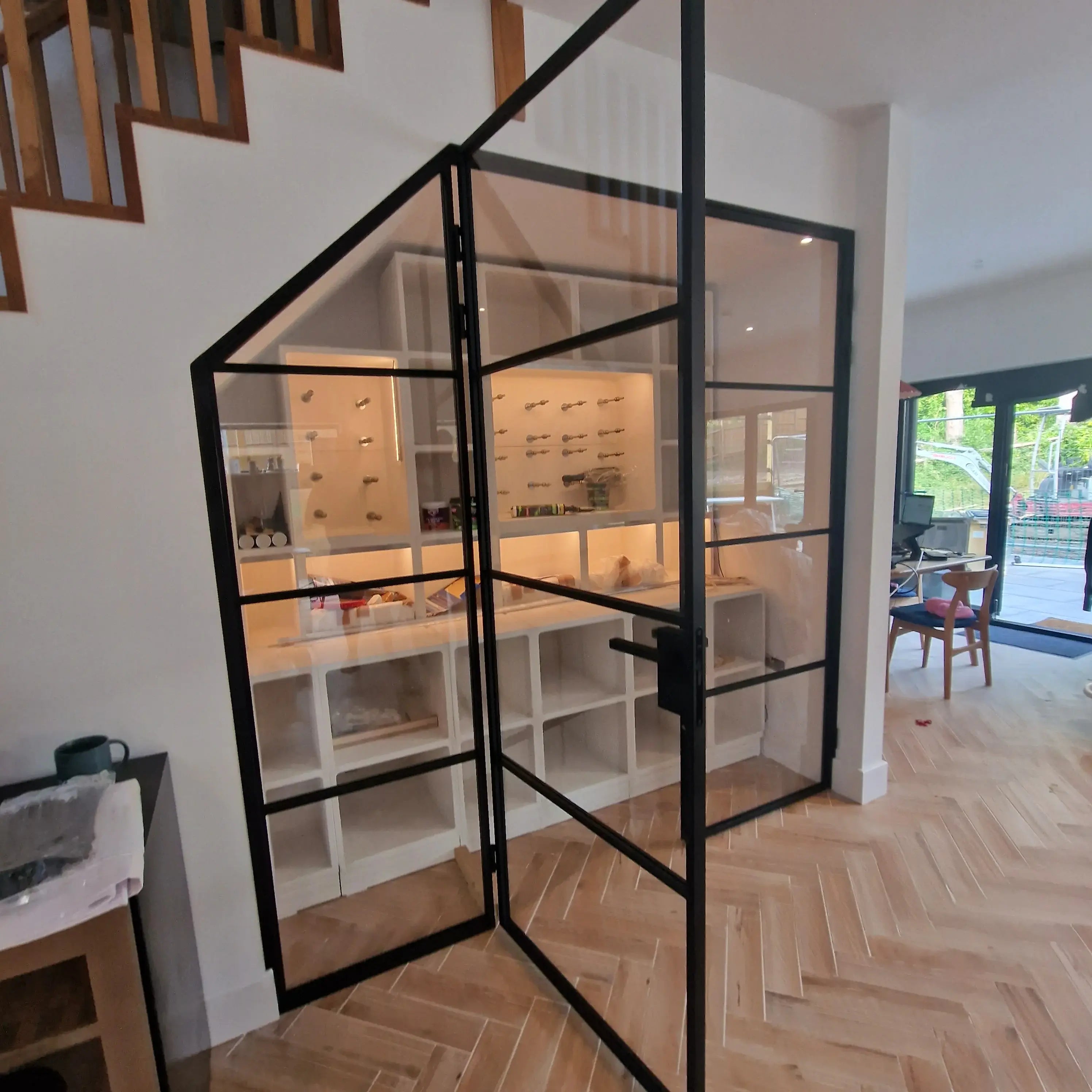 Double hinged black metal frame glass door in modern home with wooden herringbone floor