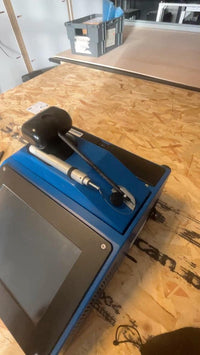 Blue industrial machine with digital display on wooden workbench in workshop setting