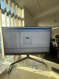 Office desk with LG monitor displaying PRODIN software interface, glass stand, and window blinds