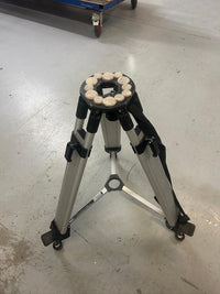 Silver tripod with black accents and circular foam pads on top, placed on a concrete floor.