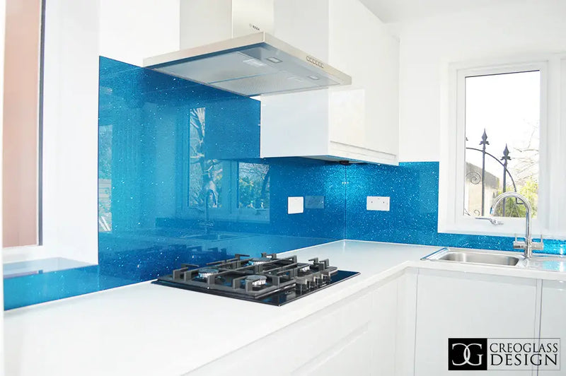 Modern kitchen with sparkling blue glass backsplash, white cabinets, gas stove, and stainless steel sink