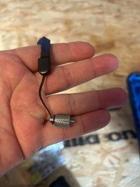 Hand holding small metal tool with blue lanyard, likely for glass installation or adjustment.