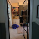 Open black framed glass interior door revealing cozy room with bookshelves, blue star-patterned bean bag, and rug