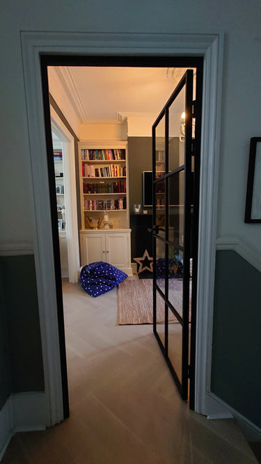 Open black framed glass interior door revealing cozy room with bookshelves, blue star-patterned bean bag, and rug