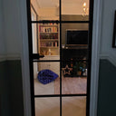 Black framed glass hinged interior door revealing a cozy living room with bookshelf, TV, and blue star-patterned bean bag