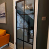 Modern black framed glass hinged door with white frame in home interior with orange couch