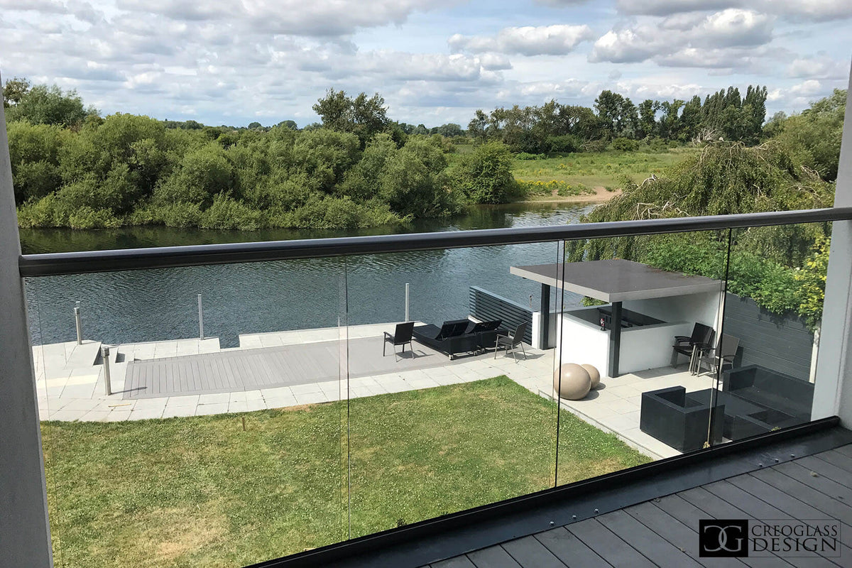 Modern balcony with glass railing overlooking a lake and greenery