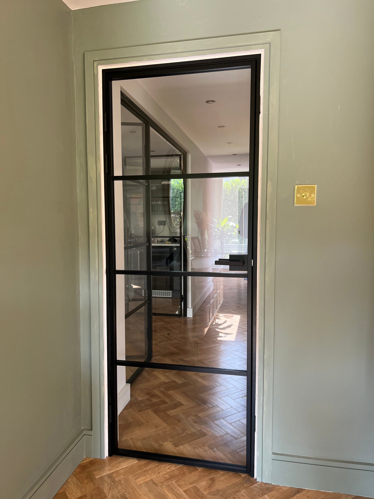 Black framed glass door with horizontal bars in modern hallway with herringbone wood floor and gray walls