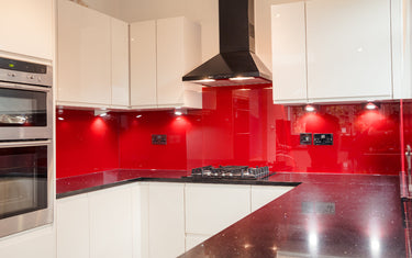 Modern kitchen with red backsplash, white cabinets, and stainless steel appliances.