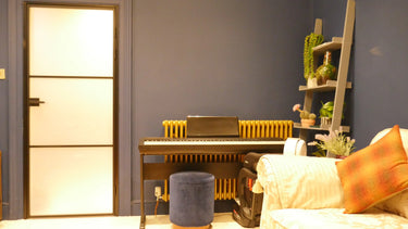 Indoor room with a dark blue wall, digital piano, blue velvet stool, modern frosted glass door, and cozy sofa