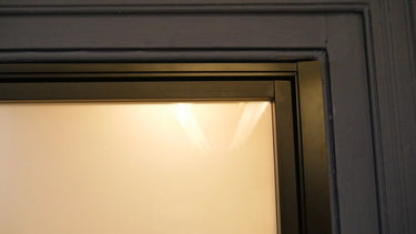 Close-up of a hinged door frame with frosted glass and matte black metal edging