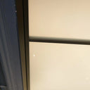 Close-up of hinged frosted glass door framed in black metal, adjacent to blue doorframe and tiled floor